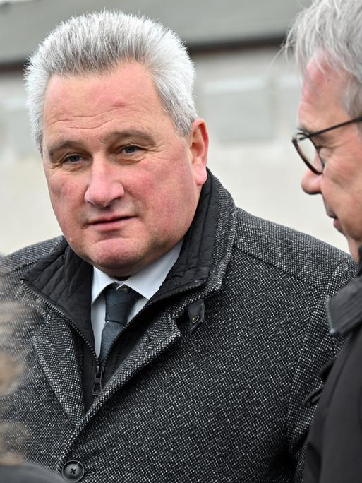 Jens-Christian Wagner, Direktor der Stiftung Gedenkstätten Buchenwald und Mittelbau-Dora, steht auf dem Appellplatz in der Gedenkstätte Buchenwald zwischen zwei Personen und schaut in die Kamera. Er trägt einen dicken grauen Wintermantel.