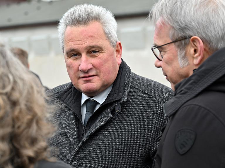 Jens-Christian Wagner, Direktor der Stiftung Gedenkstätten Buchenwald und Mittelbau-Dora, steht auf dem Appellplatz in der Gedenkstätte Buchenwald zwischen zwei Personen und schaut in die Kamera. Er trägt einen dicken grauen Wintermantel.