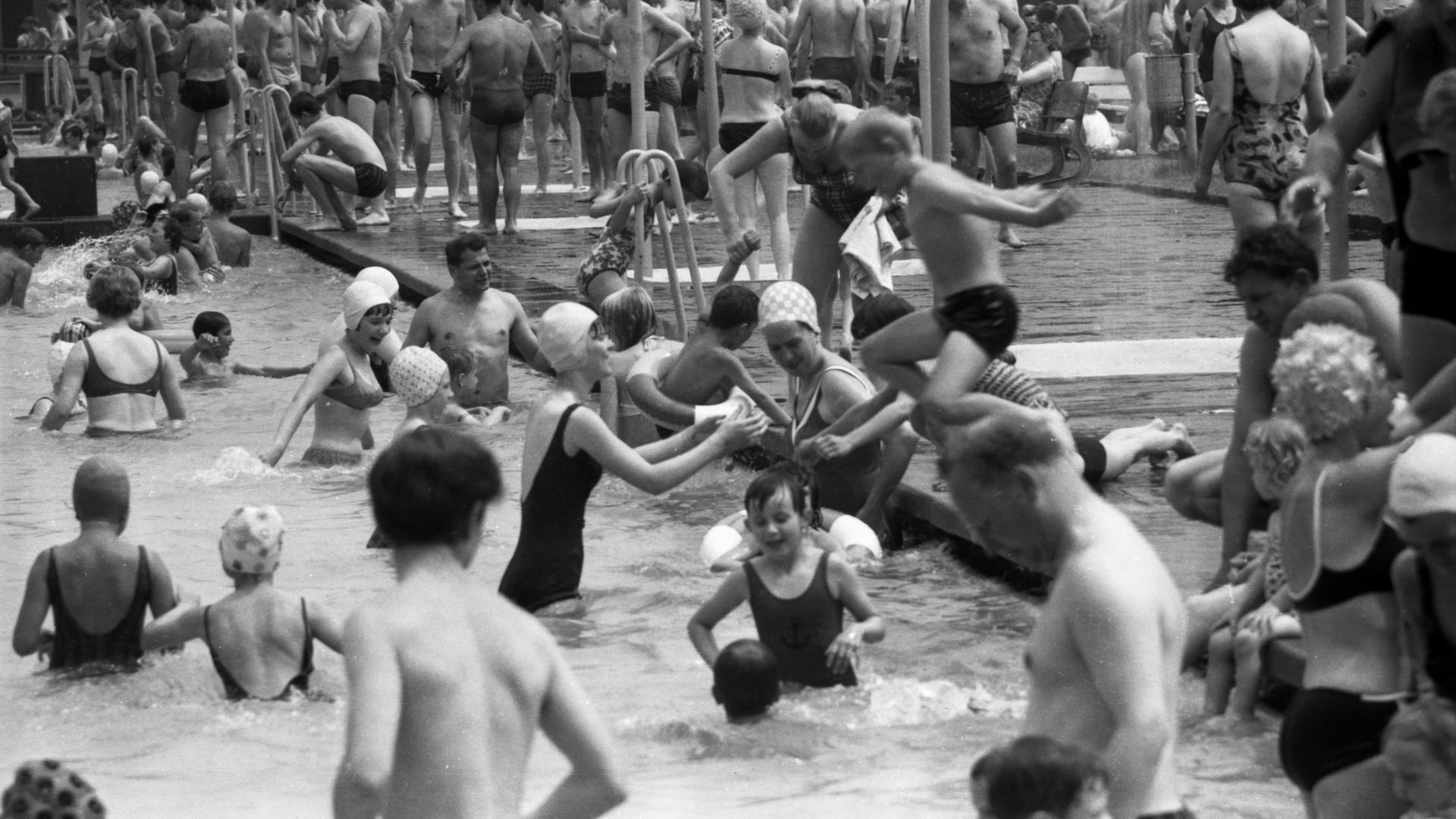 Schwarz-weiß Foto: Viele Menschen im Freibad, das Becken ist voll.