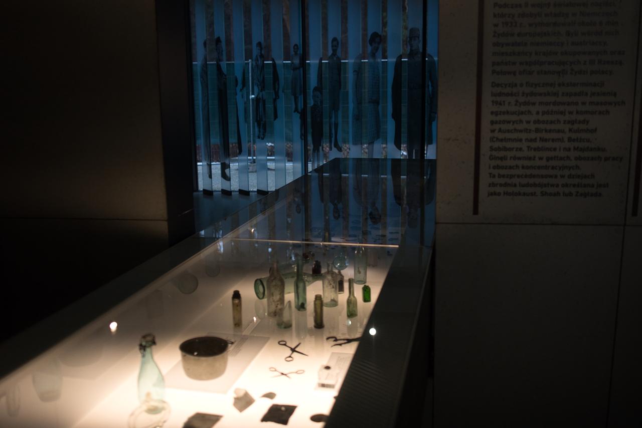 Eine beleuchtete Vitrine in einem dunklen Ausstellungsraum zeigt ausgegrabene Objekte aus dem Wald bei Sobibor