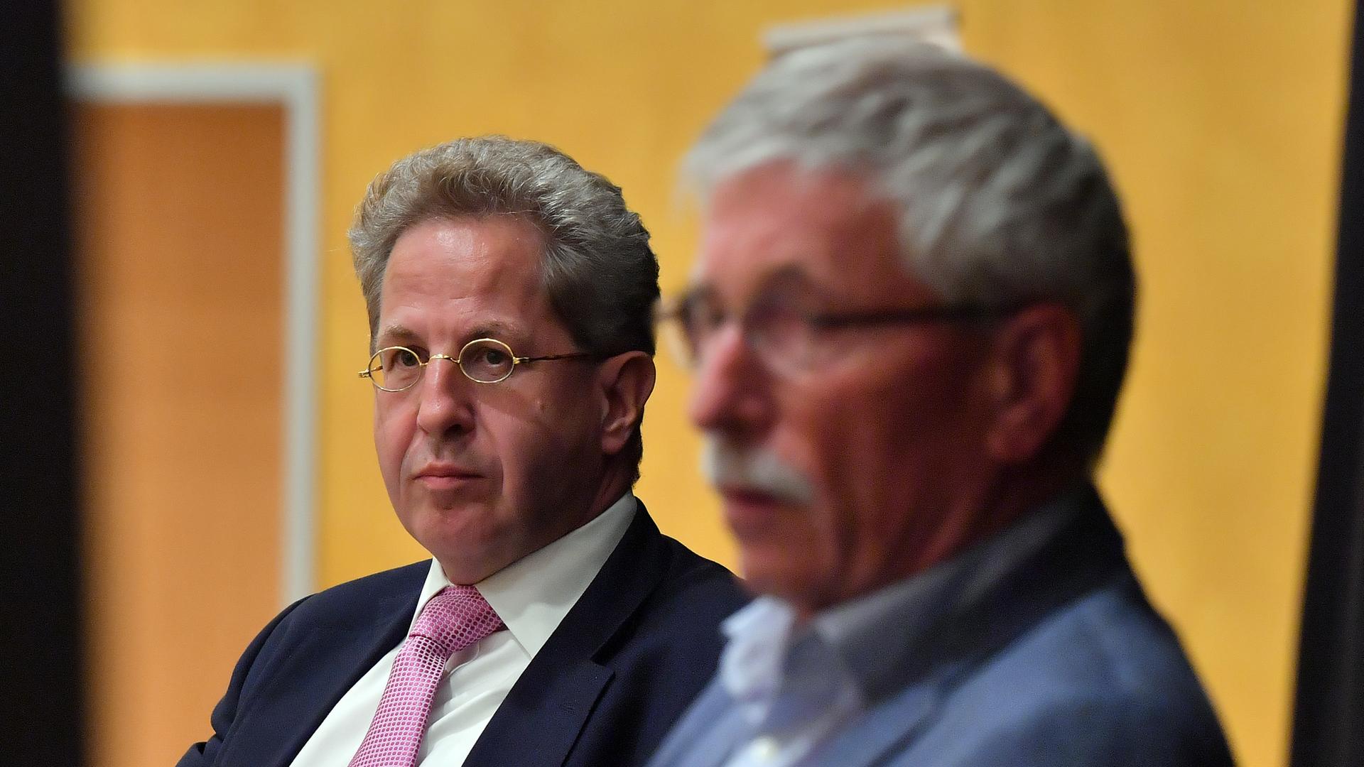 Zwei Männer sitzen auf einer Veranstaltung. Hans-Georg Maaßen (hinten) ist scharf zu sehen, Thilo Sarrazin im Vordergrund verschwommen. 