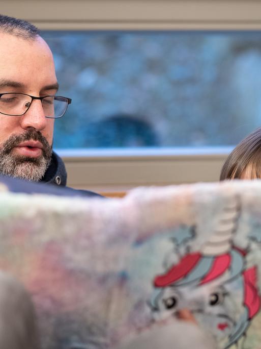 Ein Erzieher liest einem Kind in einer Kita aus einem Buch mit einem Einhorn auf der Titelseite vor. 