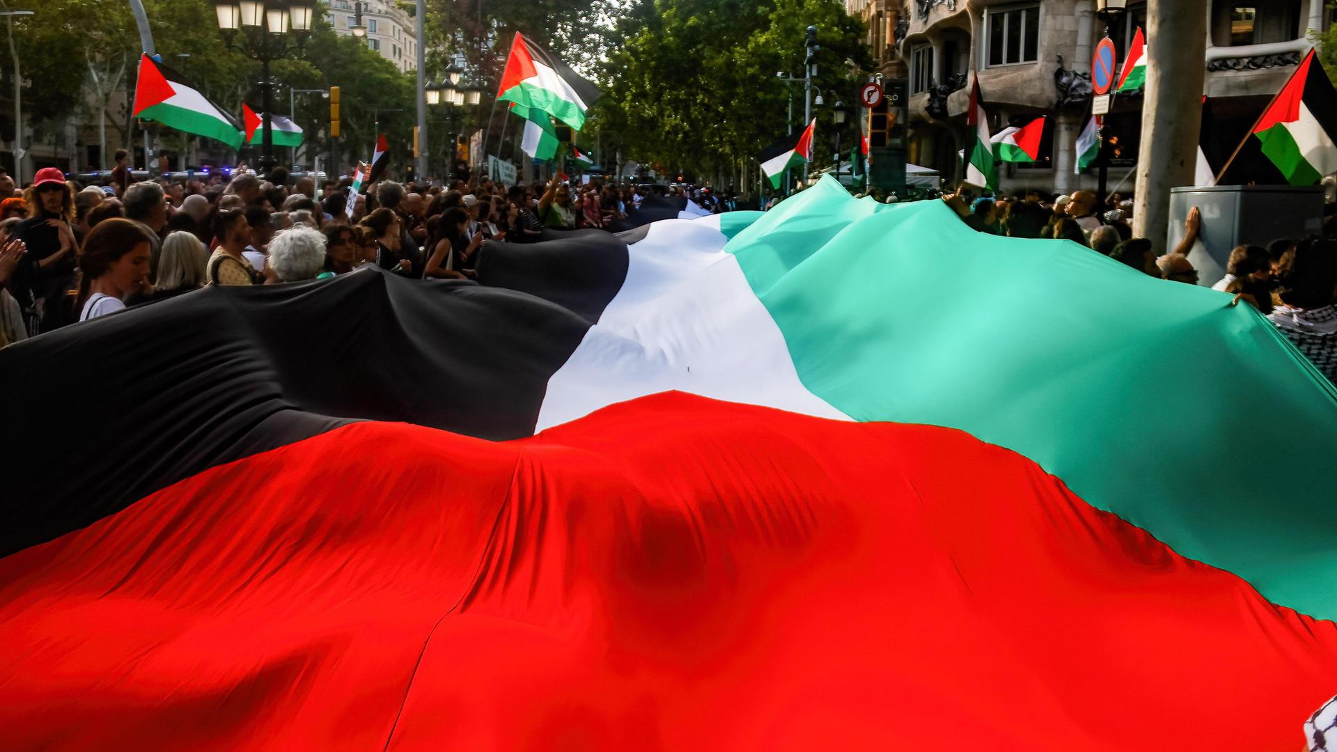 Menschen tragen eine große palästinensische Flagge durch die Straßen von Barcelona