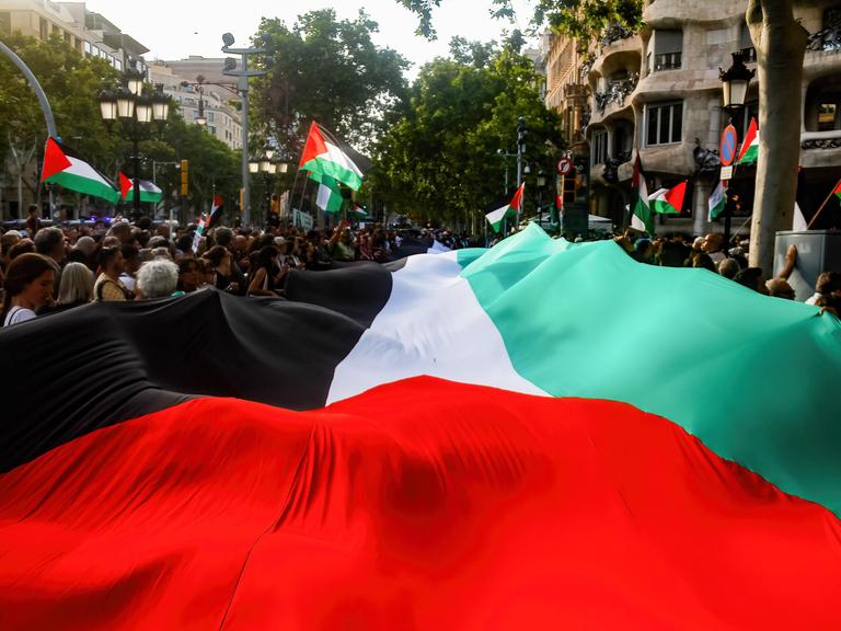 Menschen tragen eine große palästinensische Flagge durch die Straßen von Barcelona