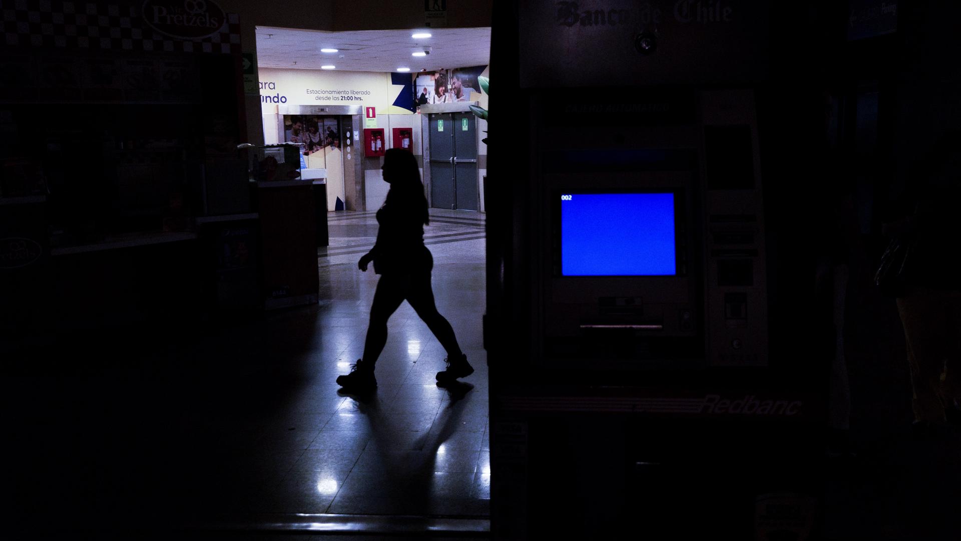 Eine Frau geht während eines Stromausfalls durch eine Shopping Mall in Santiago: Weite Teile der Szene sind dunkel, nur wenige Lampen leuchten, die Frau ist als Schatten zu sehen.