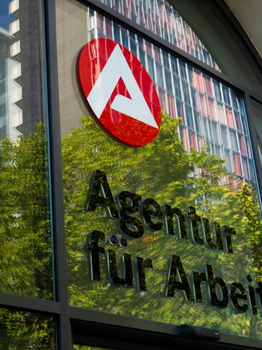 07.09.2023, Berlin. Der Schriftzug "Agentur fuer Arbeit" und das Logo der Agentur sind an einem Jobcenter in Kreuzberg zu sehen. In der Scheibe des Eingangs spiegeln sich dabei die Blaetter von Baeumen und umliegende Gebaeude. Foto: Wolfram Steinberg/dpa