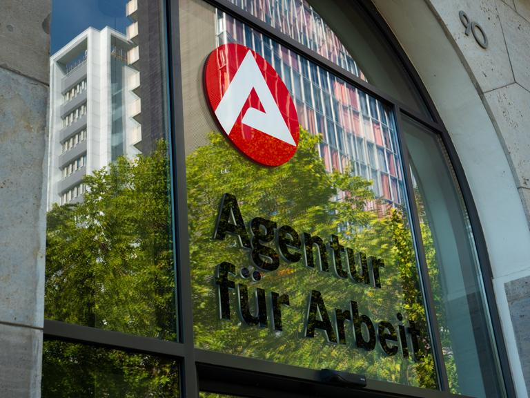 07.09.2023, Berlin. Der Schriftzug "Agentur fuer Arbeit" und das Logo der Agentur sind an einem Jobcenter in Kreuzberg zu sehen. In der Scheibe des Eingangs spiegeln sich dabei die Blaetter von Baeumen und umliegende Gebaeude. Foto: Wolfram Steinberg/dpa