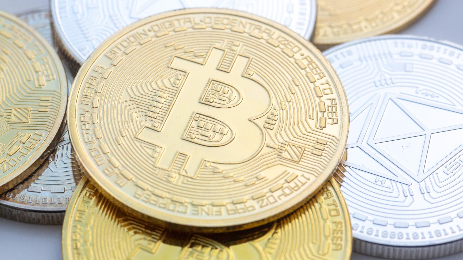 Münzen mit den Symbolen von Bitcoin (M) und Ethereum sind auf einem Tisch angeordnet.