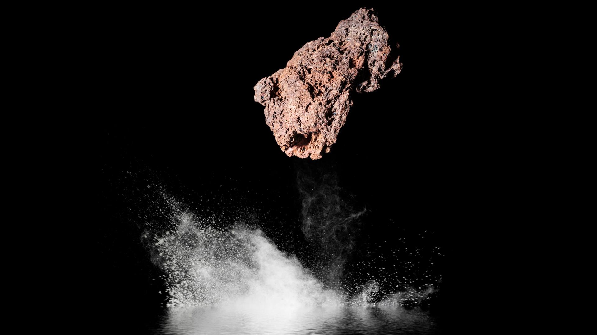 Ein Steinmeteorit aus dem Weltall, er fällt in schwarzes Wasser bei Nacht.
