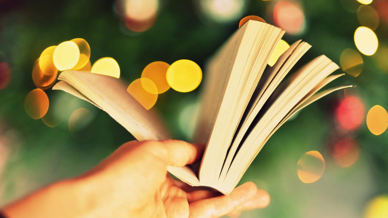 Eine Hand hält ein aufgeschlagenes Buch vor verschwommenem Hintergrund, der so aussieht, als sei es ein Weihnachtsbaum mit Beleuchtung.