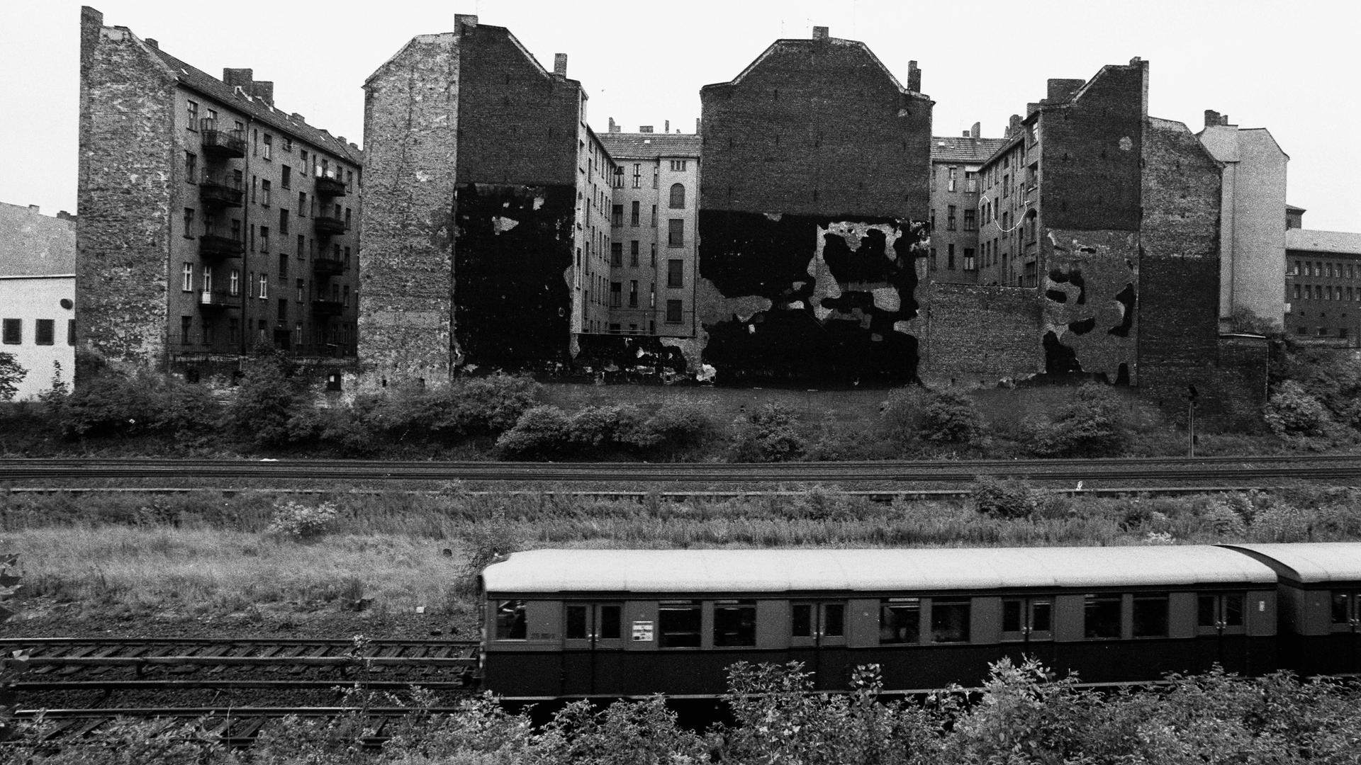 Eine S-Bahn fährt an Häusern vorbei. Es sind alte Häuser im damaligen Ostberlin.