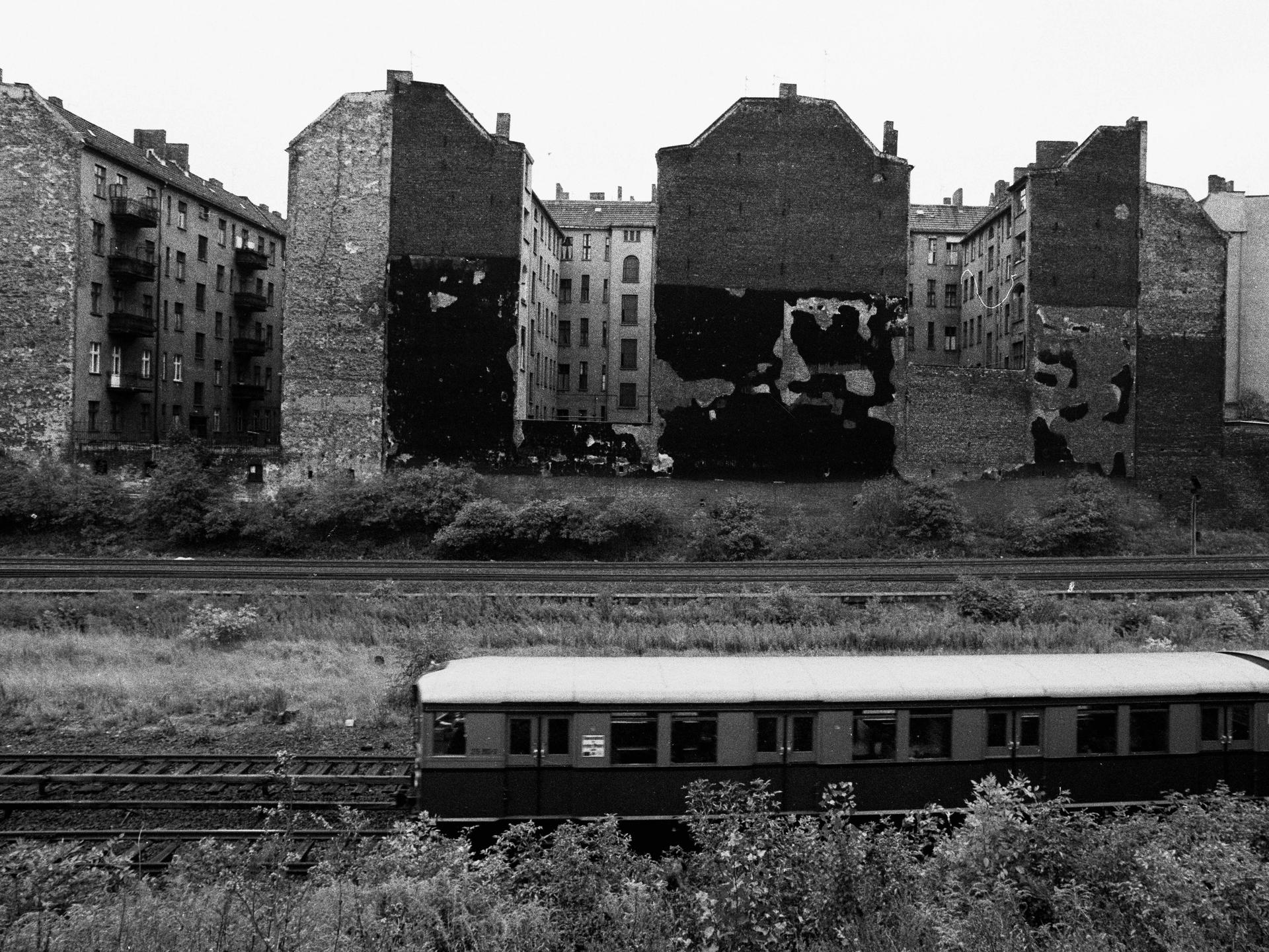 Eine S-Bahn fährt an Häusern vorbei. Es sind alte Häuser im damaligen Ostberlin.