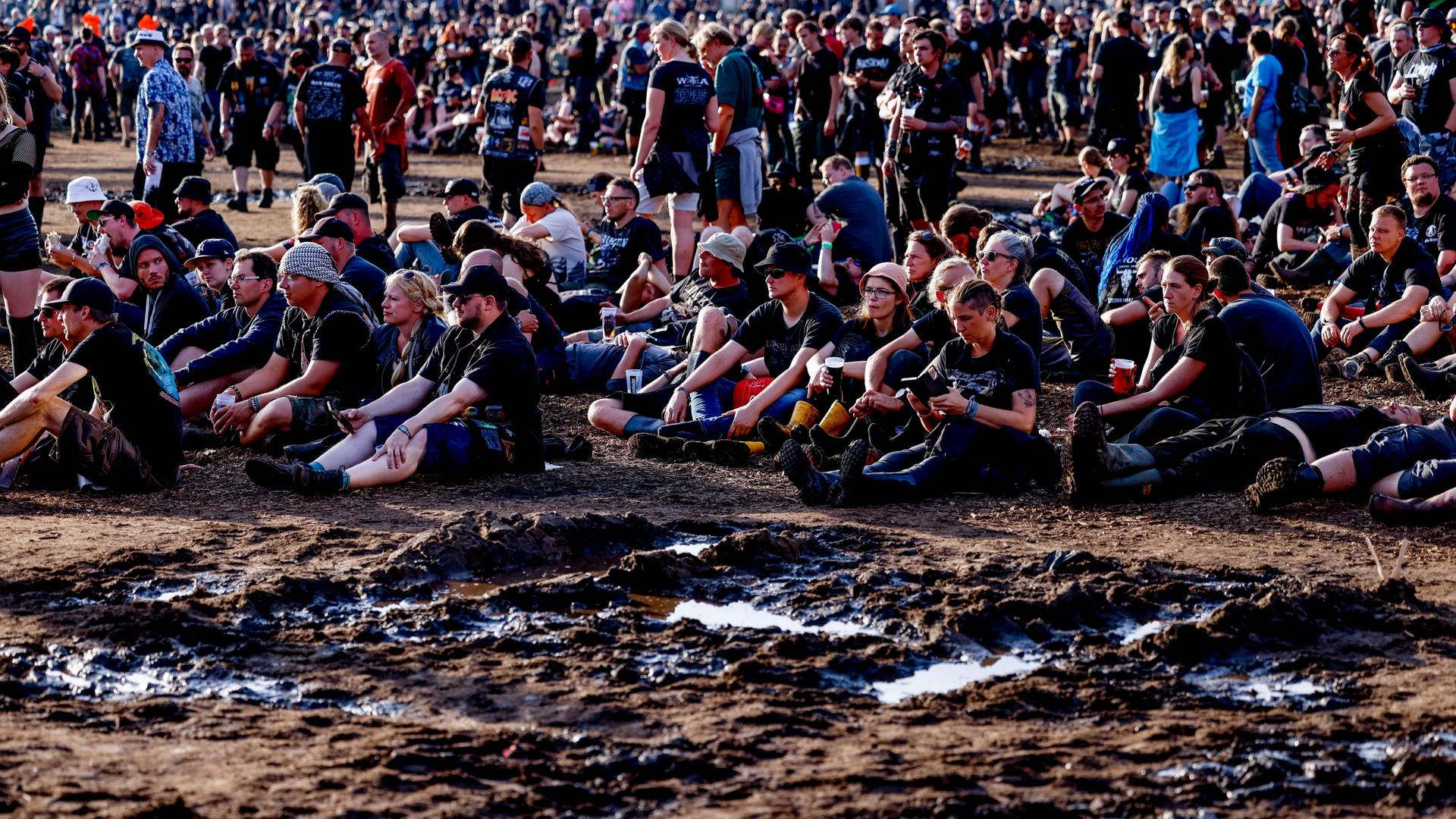 Festivalbesucher sitzen beim Wacken Open Air neben den abtrocknenden Schlammflächen auf dem Veranstaltungsgelände und hören den Auftritten der Bands zu. Festivalbesucher sitzen beim Wacken Open Air neben den abtrocknenden Schlammflächen auf dem Veranstaltungsgelände und hören den Auftritten der Bands zu.
