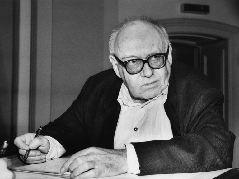 Das Foto zeigt den Dichter Ernst Jandl an einem Tisch sitzend mit Notizblock und Stift in der Hand.