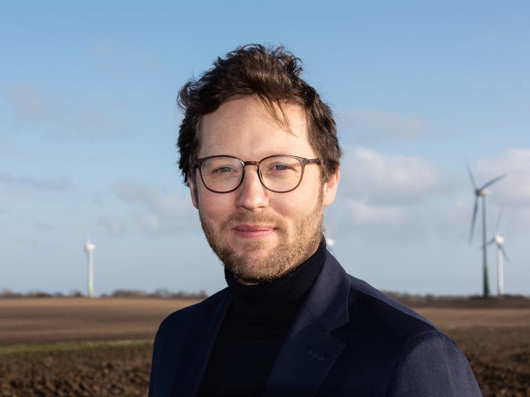 Porträt des deutsche Politikers Jan Philipp Albrecht, er steht auf einem Feld vor einer Windkraftanlage.