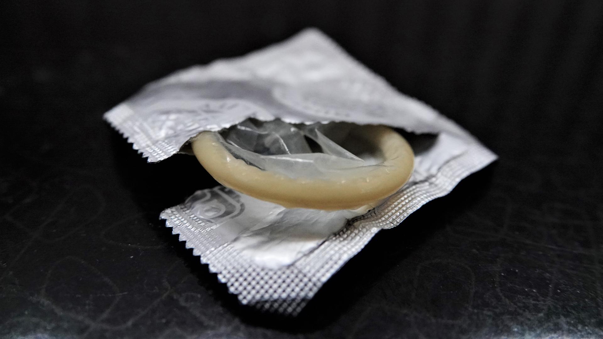 Eine geöffnete Kondompackung liegt neben einem Bett auf einem Nachttisch. Eine geöffnete Kondompackung liegt neben einem Bett auf einem Nachttisch.