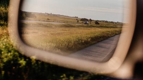 Der Seitenspiegel eines Autos, man sieht eine Landschaft.