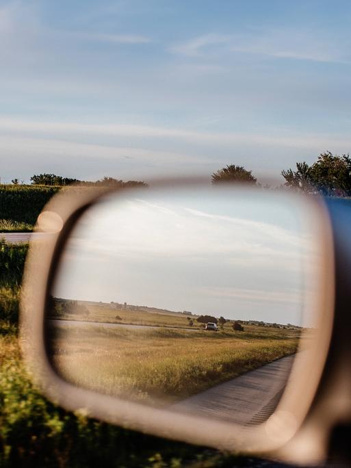 Der Seitenspiegel eines Autos, man sieht eine Landschaft.