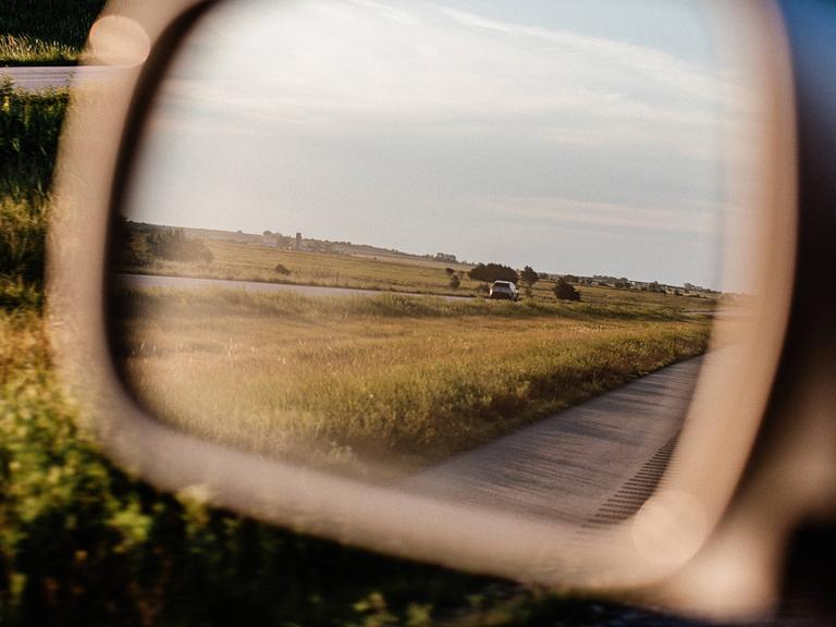 Der Seitenspiegel eines Autos, man sieht eine Landschaft.