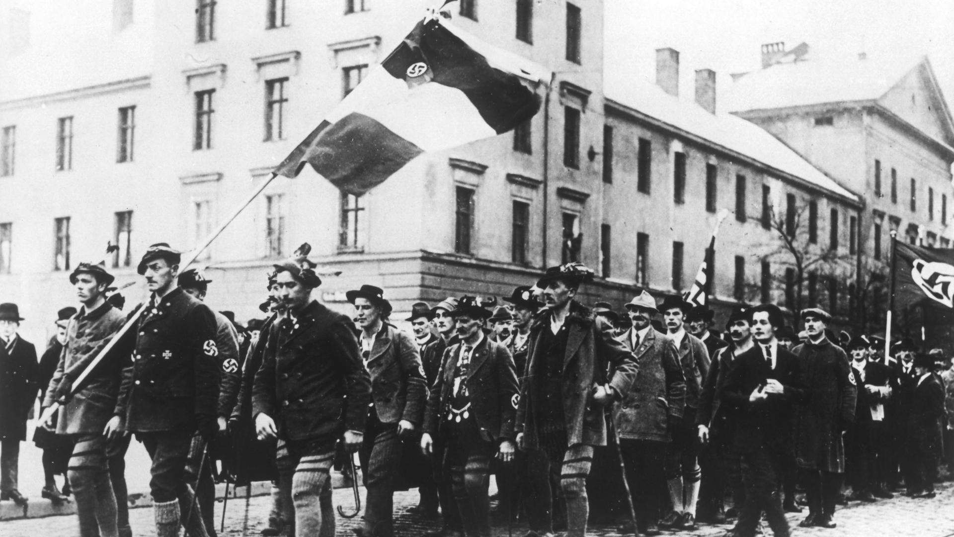Ein historisches Foto zeigt einen Menschenzug mit Fahnenträgern beim 1. Parteitag der NSDAP.