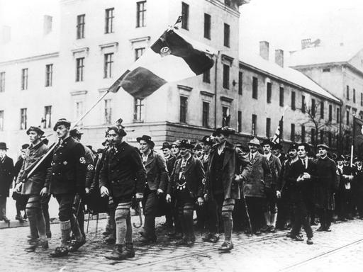 Ein historisches Foto zeigt einen Menschenzug mit Fahnenträgern beim 1. Parteitag der NSDAP.