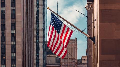 Blick in die Wall Street, an einem Gebäude hängt die amerikanische Flagge.