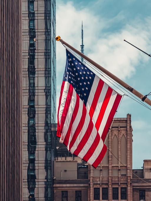 Blick in die Wall Street, an einem Gebäude hängt die amerikanische Flagge.