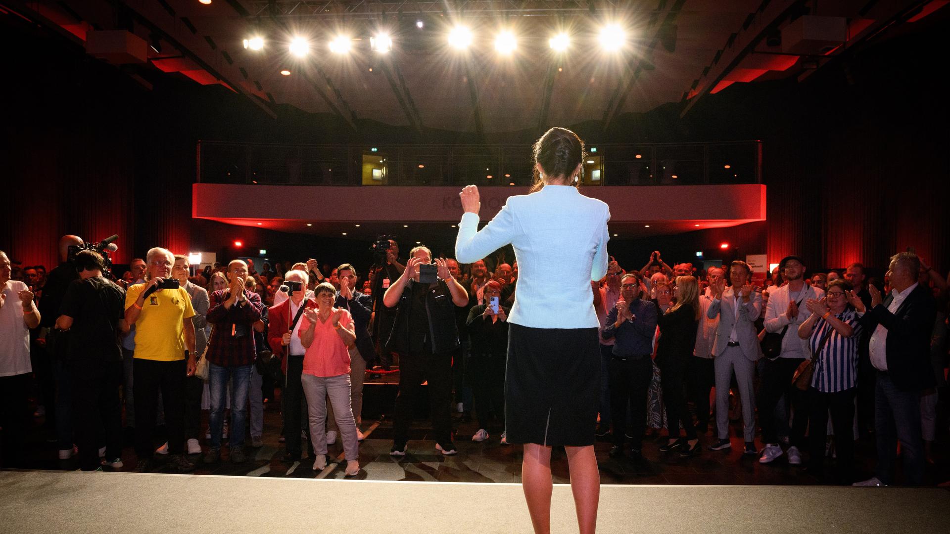 Sahra Wagenknecht steht auf einer Bühne. Vor ihr Menschen, die zujubeln. Darüber Scheinwerfer, die Wagenknecht ins Rampenlicht rücken.