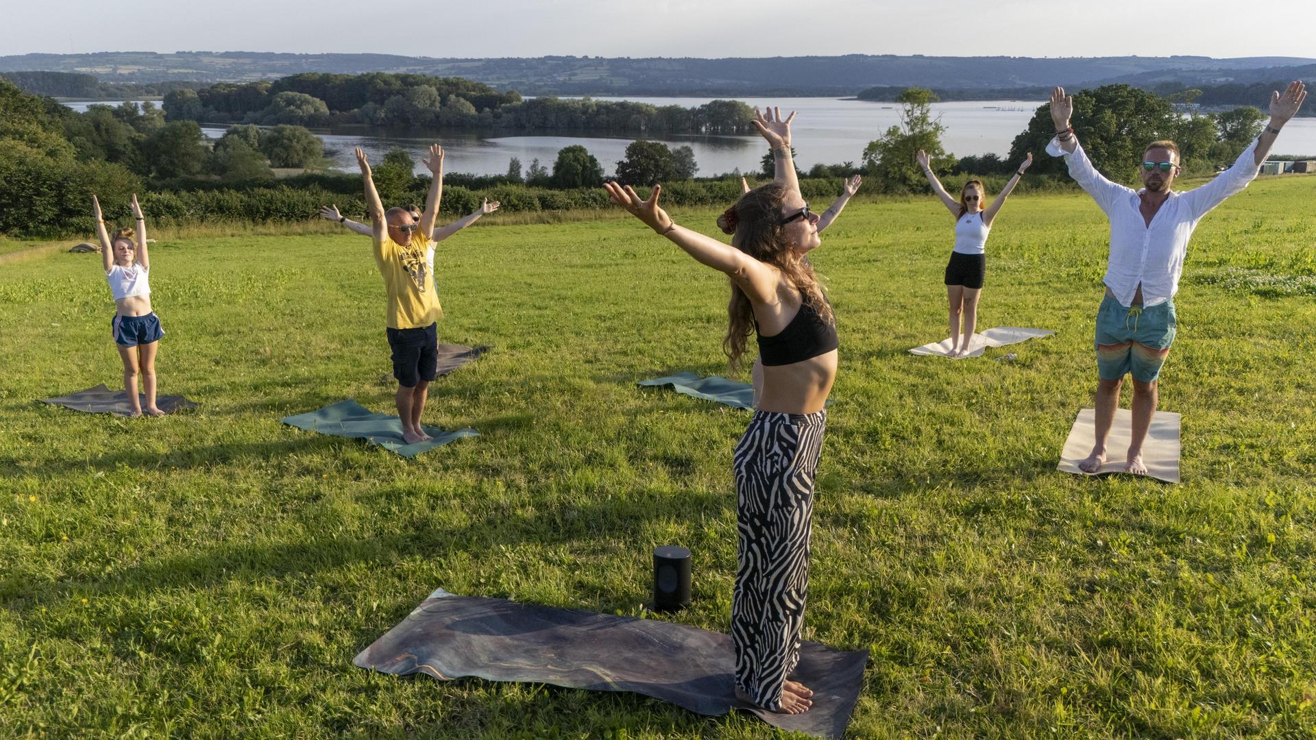 Eine Gruppe Männer und Frauen macht Yoga bei einem See.