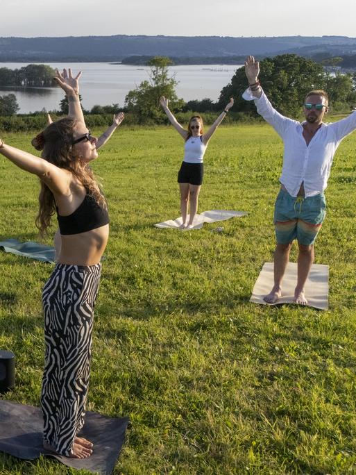 Eine Gruppe Männer und Frauen macht Yoga bei einem See.