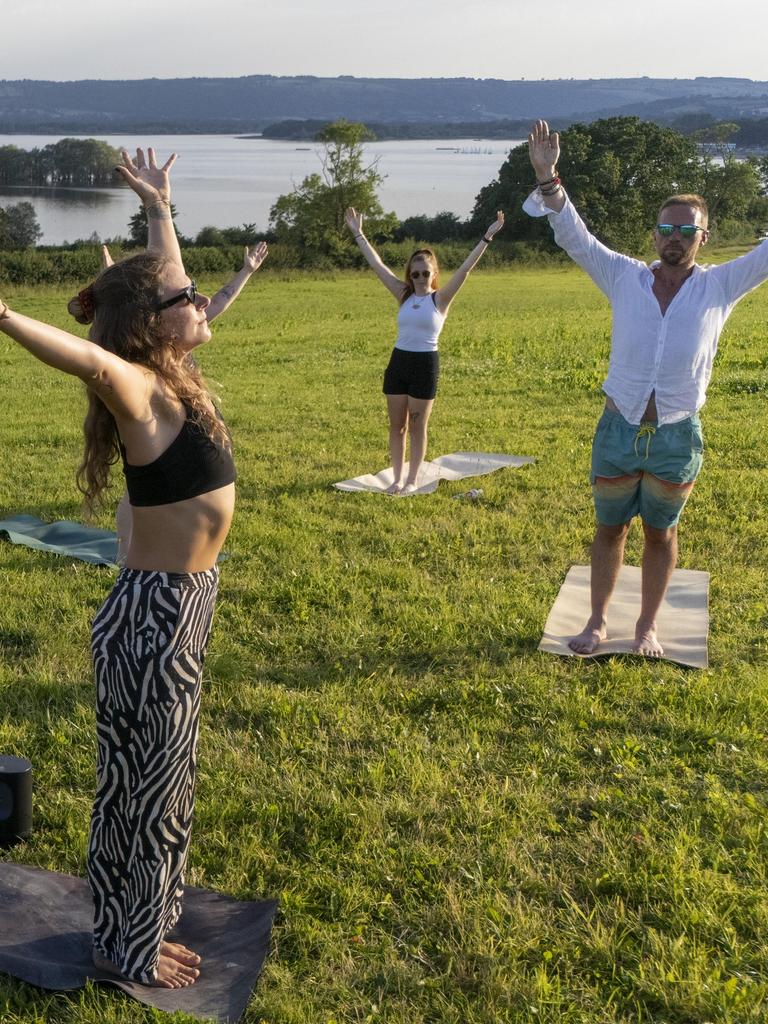 Eine Gruppe Männer und Frauen macht Yoga bei einem See.