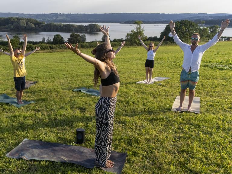 Eine Gruppe Männer und Frauen macht Yoga bei einem See.