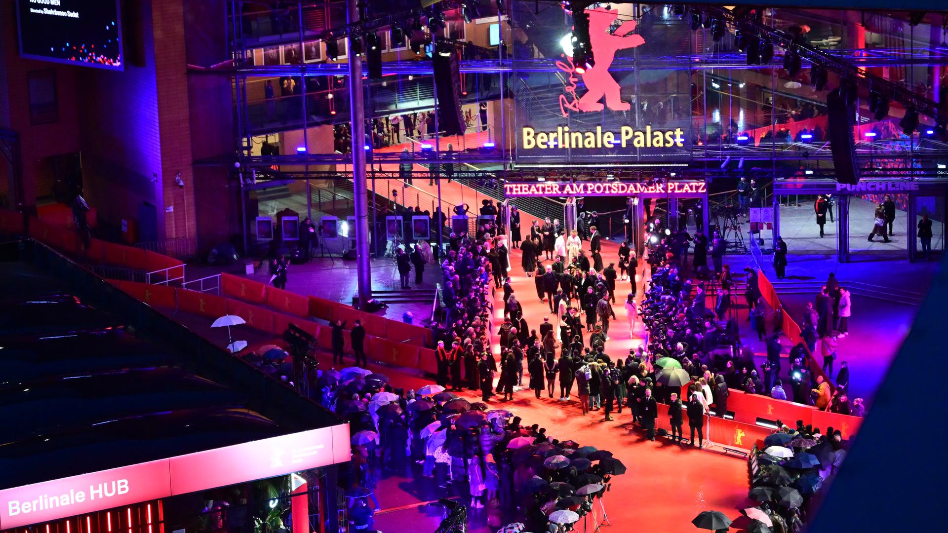 Das Bild zeigt zahlreiche Gäste am Rande eines und auf einem Roten Teppich bei Nacht. Dahinter ist in großen Leuchtbuchstaben der Schriftzug "Berlinale Palast" zu sehen. Das Bild zeigt zahlreiche Gäste am Rande eines und auf einem Roten Teppich bei Nacht. Dahinter ist in großen Leuchtbuchstaben der Schriftzug "Berlinale Palast" zu sehen.