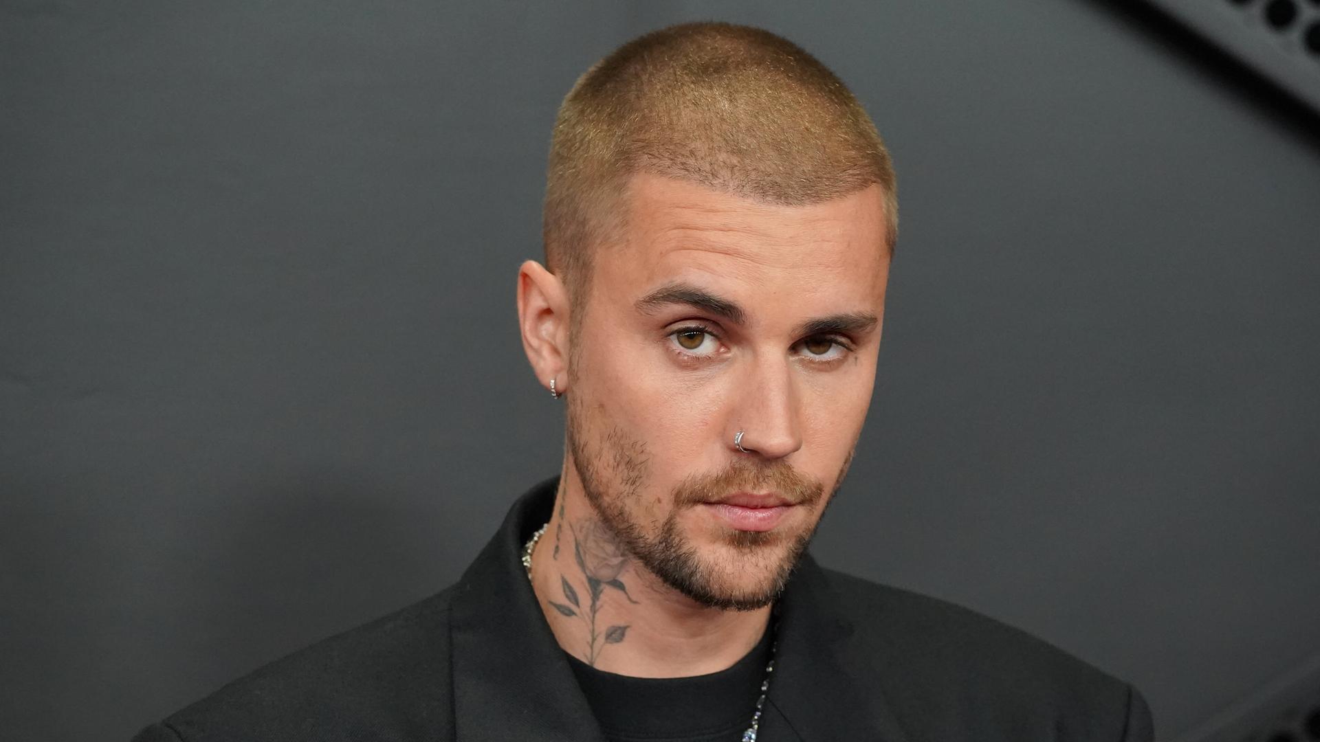 Ein Foto von Justin Bieber vor dunklem Hintergrund. Der 32-Jährige hat kurz geschorene Haare und eine Rose auf die Seite seines Halses tätowiert.
