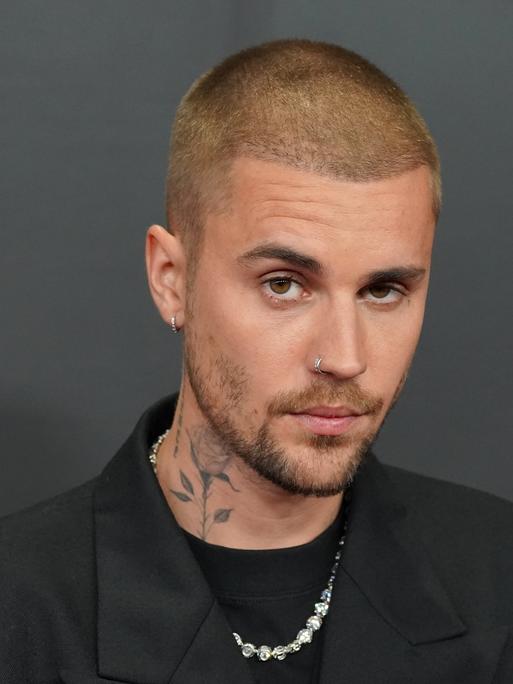 Ein Foto von Justin Bieber vor dunklem Hintergrund. Der 32-Jährige hat kurz geschorene Haare und eine Rose auf die Seite seines Halses tätowiert.