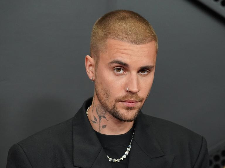 Ein Foto von Justin Bieber vor dunklem Hintergrund. Der 32-Jährige hat kurz geschorene Haare und eine Rose auf die Seite seines Halses tätowiert.