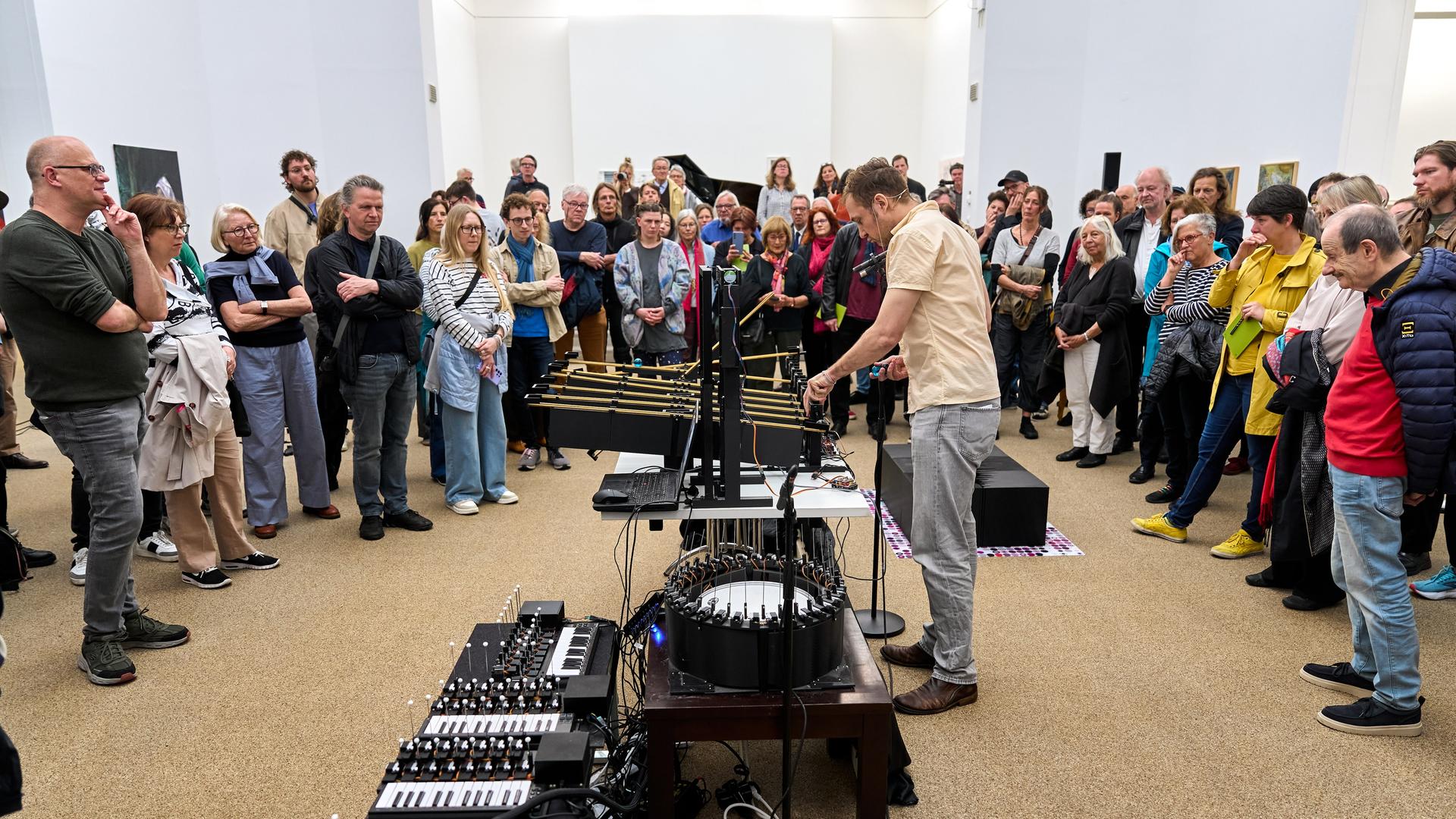 Ein Mann operiert an einem phantasievollen klingenden Instrumentarium, während das Publikum um ihn herum steht
