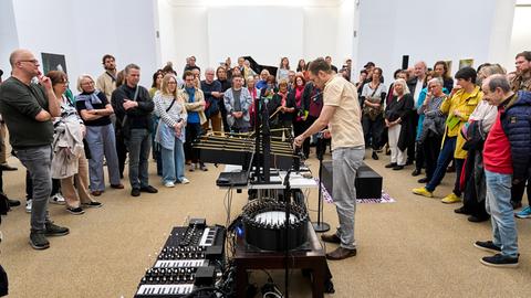 Ein Mann operiert an einem phantasievollen klingenden Instrumentarium, während das Publikum um ihn herum steht