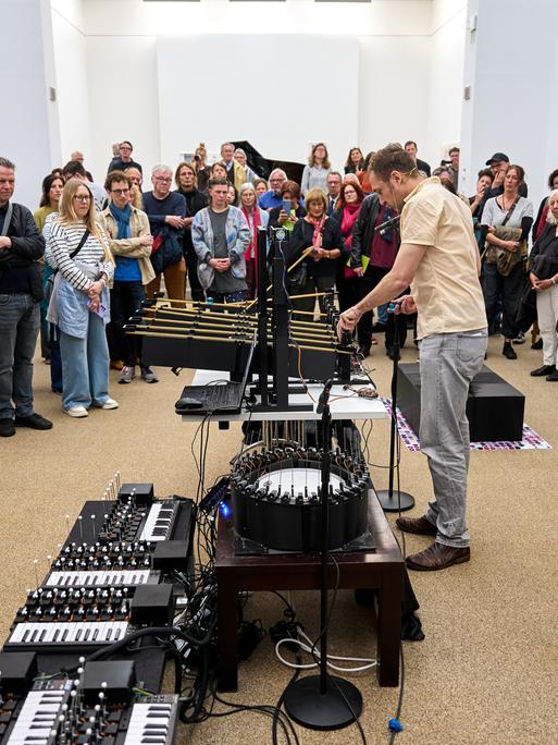 Ein Mann operiert an einem phantasievollen klingenden Instrumentarium, während das Publikum um ihn herum steht