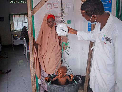 Eine Somalierin steht neben ihrem Sohn, der von einem Mitarbeiter einer Hilfsorganisation gewogen wird
