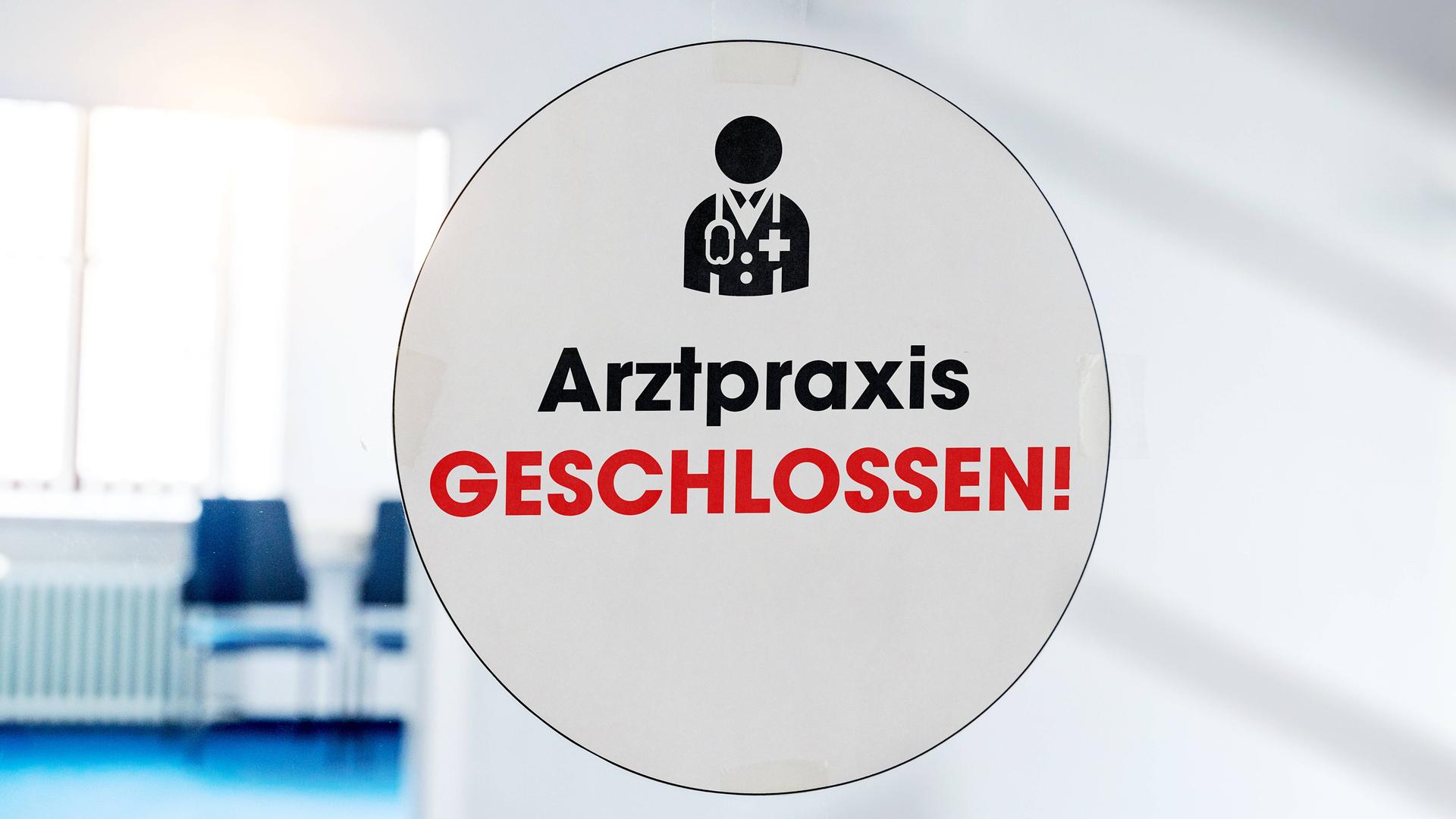 Ein Schild mit der Aufschrift "Arztpraxis geschlossen" an der Glastür einer Praxis.