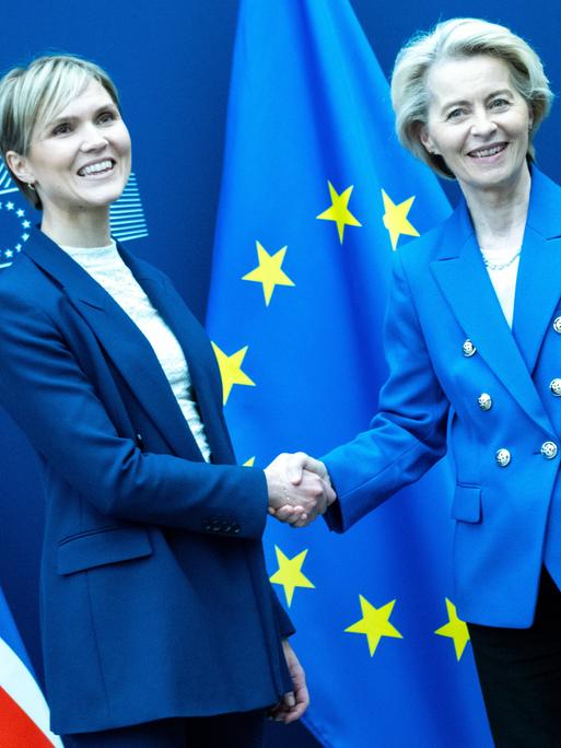 Die isländische Ministerpräsidentin Kristrun Frostadottir und EU-Kommissionschefin Ursula von der Leyen geben sich vor den Fahnen Islands und der EU die Hand