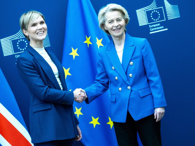 Die isländische Ministerpräsidentin Kristrun Frostadottir und EU-Kommissionschefin Ursula von der Leyen geben sich vor den Fahnen Islands und der EU die Hand