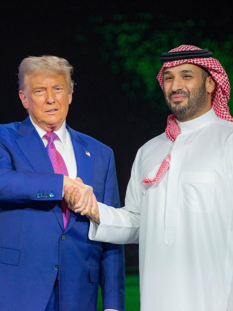 US-Präsident Trump in einem meerblauen Anzug schüttelt die Hand des saudischen Kronprinzen Mohammed bin Salman, der in traditionellem weissen Gewandt und einem Rot-weissen Ghutra auf dem Kopf auf der Bühne steht. 