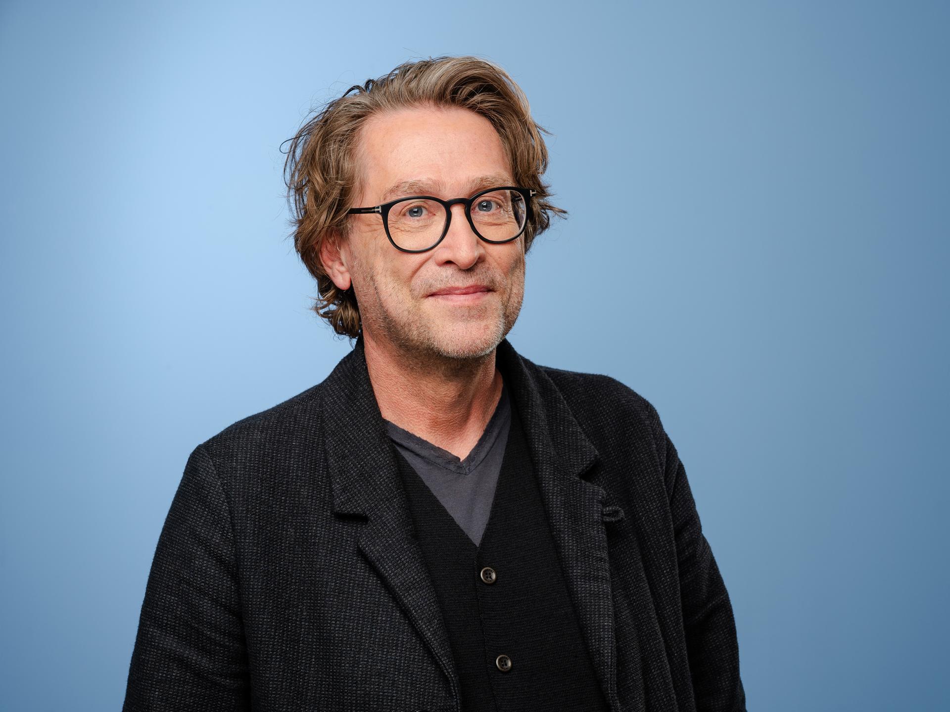 Jan Weiler posiert mit einem Jackett und Brille im Rahmen der MDR-Talkshow Riverboat in Leipzig vor einem hellblauen Hintergrund für ein Foto. Jan Weiler posiert mit einem Jackett und Brille im Rahmen der MDR-Talkshow Riverboat in Leipzig vor einem hellblauen Hintergrund für ein Foto.