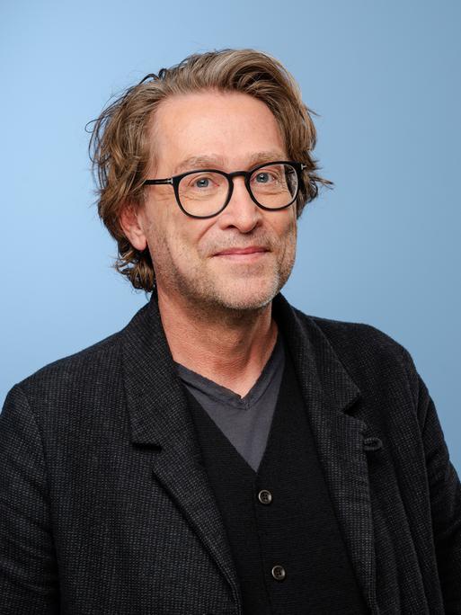 Jan Weiler posiert mit einem Jackett und Brille im Rahmen der MDR-Talkshow Riverboat in Leipzig vor einem hellblauen Hintergrund für ein Foto. Jan Weiler posiert mit einem Jackett und Brille im Rahmen der MDR-Talkshow Riverboat in Leipzig vor einem hellblauen Hintergrund für ein Foto.