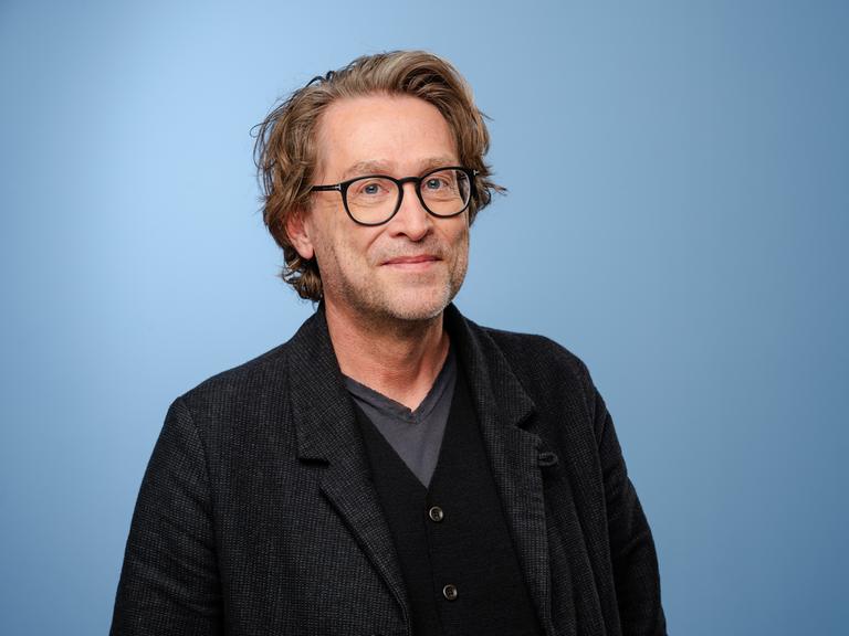 Jan Weiler posiert mit einem Jackett und Brille im Rahmen der MDR-Talkshow Riverboat in Leipzig vor einem hellblauen Hintergrund für ein Foto. Jan Weiler posiert mit einem Jackett und Brille im Rahmen der MDR-Talkshow Riverboat in Leipzig vor einem hellblauen Hintergrund für ein Foto.
