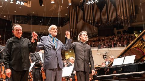 Drei Männer stehen auf der Bühne der Philharmonie und verbeugen sich.