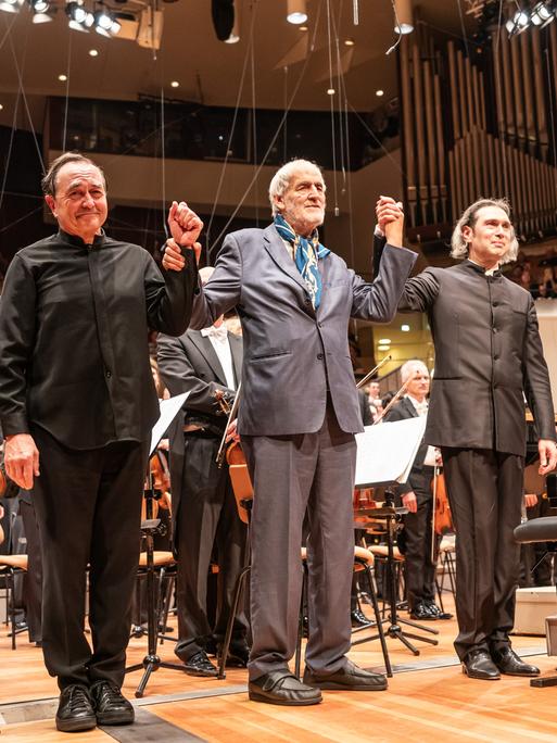 Drei Männer stehen auf der Bühne der Philharmonie und verbeugen sich.