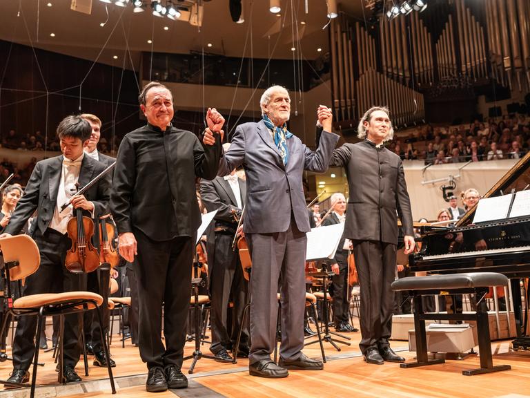 Drei Männer stehen auf der Bühne der Philharmonie und verbeugen sich.